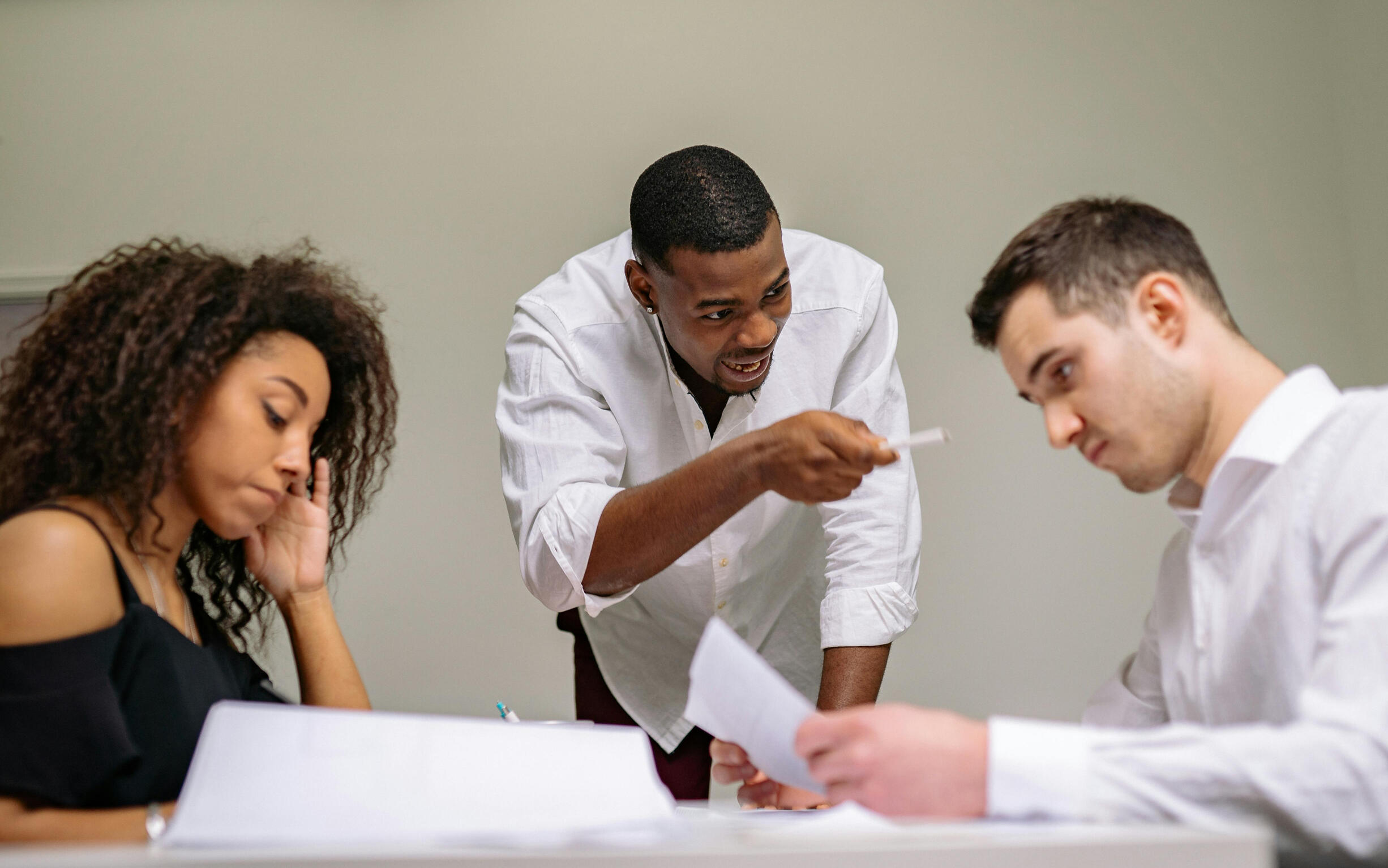 three people working together. one man is yelling at another man. woman is avoiding eye contact